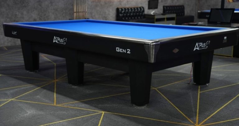Bàn Carom Aplus Gen 2 chụp góc nghiêng trong phòng tối với mặt nỉ xanh dương
